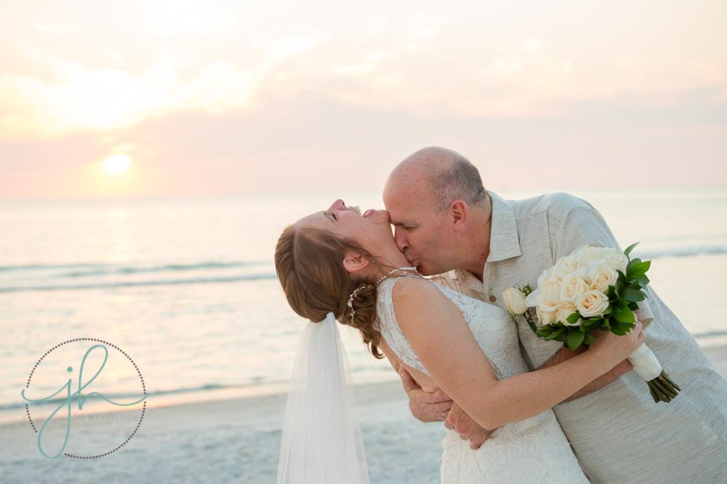 a newly married couple on the beach at sunset kissing and laughing